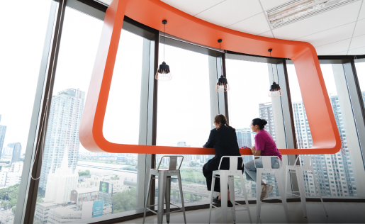 Two colleagues chat at a bright modern office bar overlooking the city