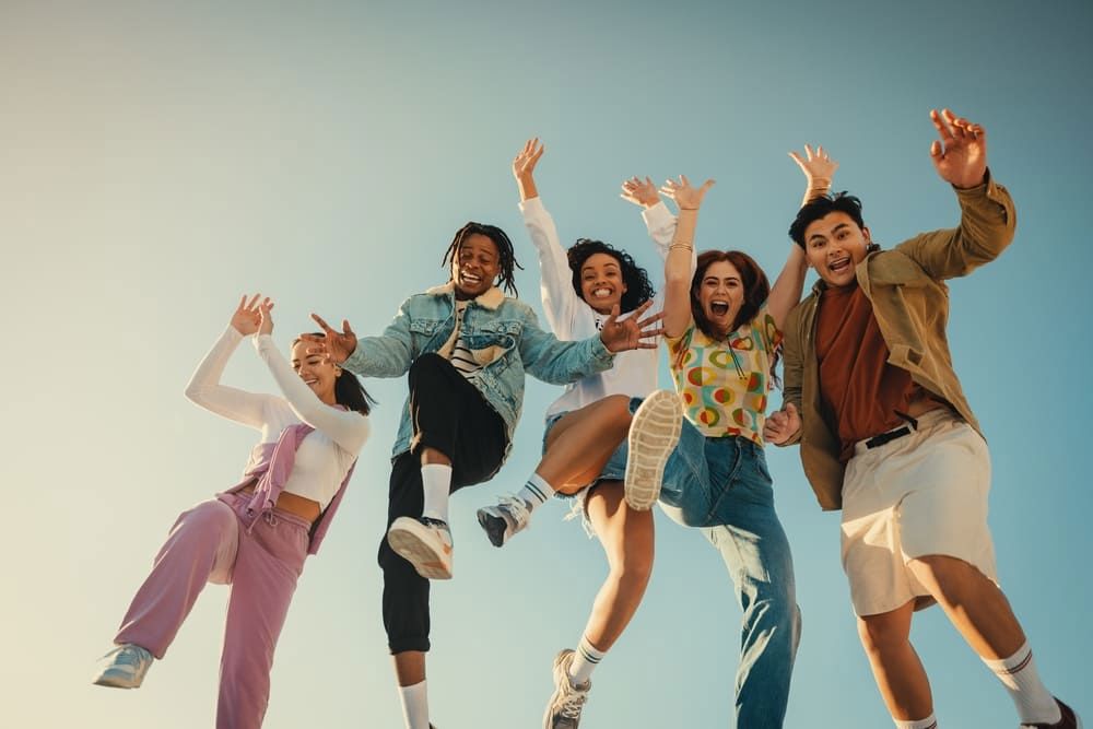 Friends jumping outdoors under a bright blue sky, symbolizing TP’s purpose driven by warmth, vibrancy, diversity, and passion.